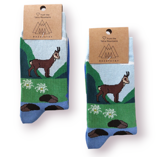 Skarpetki długie z grafiką kozicy górskiej, na tle górskiej sceneri. Łąka z potokiem, białe szarotki i błękit nieba. Na górze paierowa metka z logo firmy BazaTatry.