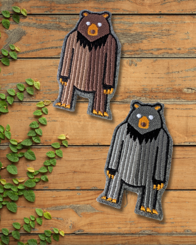 Haftowane broszki na drewnianym stole. Dwa stojące na dwóch łapach, niedźwiedzie brunatne. Brązowy i szary.