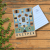Kartka pocztowa, z nowoczesną grafiką oscypków. Sery mają rożne kształty, w tle górskie szczyty i drewniana bacówka pośrodku lasu. Na dole napis: oscypek.