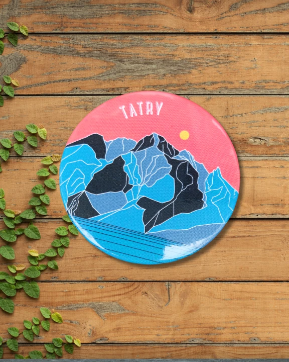 Okrągły, metalowy magnes. Nowoczesna grafika Morskiego Oka. Niebieskie szczyty górskie, na tle czerwonego nieba, na dole tafla jeziora. Napis Tatry.